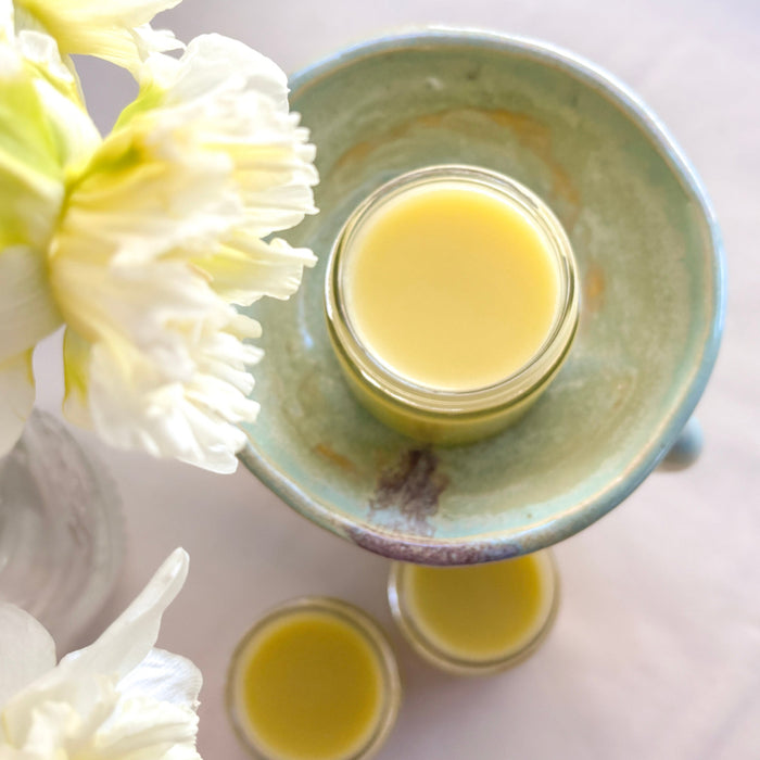 Jar of calendula salve on a ceramic plate with white flowers on a light background